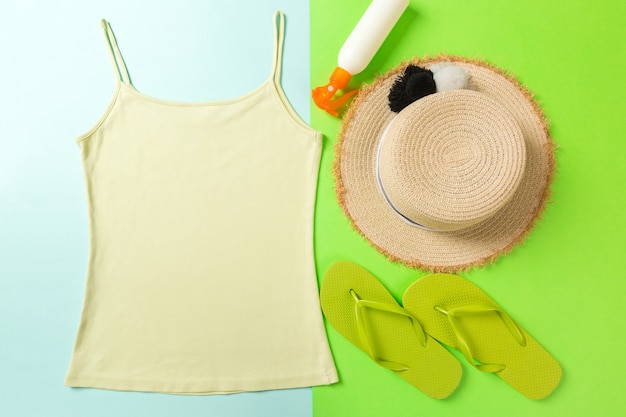 Photo summer accessories with t-shirt, seashells, sunscreen bottle and straw hat on blue and green background top view flat lay.