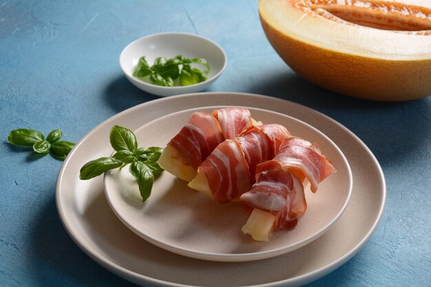 Summer appetizer with sweet melon and ham on blue background