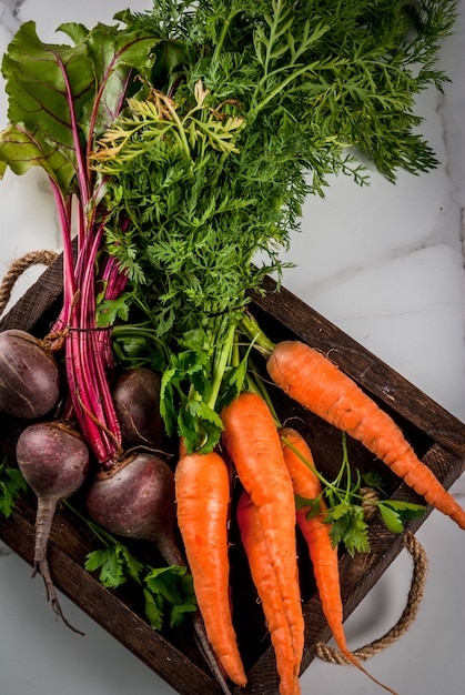 Summer, autumn harvest. Fresh organic farm vegetables in a wooden box on a white marble table - beets, carrots, parsley, tomatoes. Copy space top view