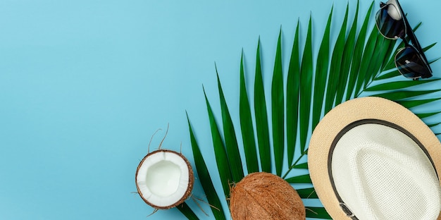 Summer background concept. Hat, sunglasses and coconut on blue background. Flat lay, copy space.