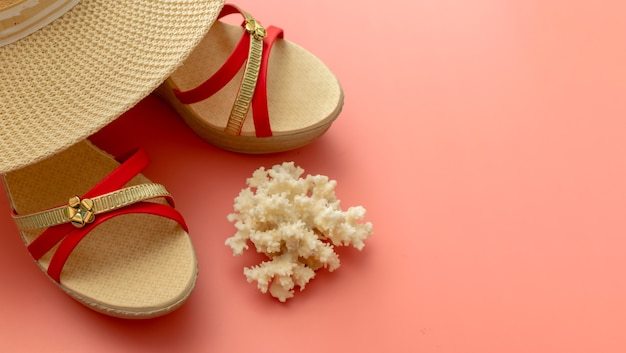 Summer background of csandals, straw hat, coral on pink background