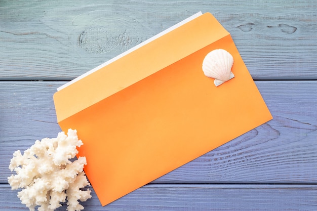 Летний фон оранжевый конверт, коралл, ракушка на синем деревянном фоне
