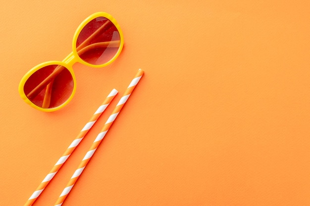 Summer background sunglasses, cocktail tubes on orange background