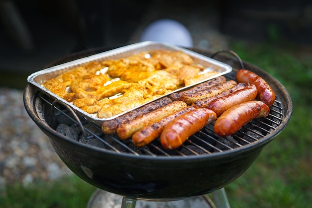 庭での夏のバーベキュー肉やソーセージを熱いグリルで焼く