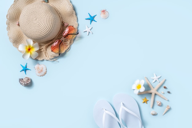Summer beach background design concept. Top view of holiday travel with shells, hat, slipper on blue background.