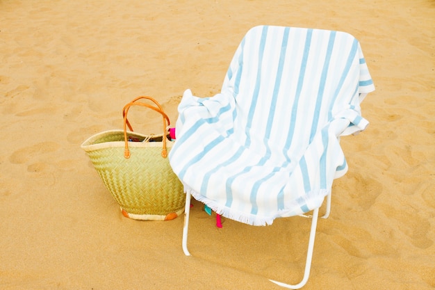 Foto sedia da spiaggia estiva con borsa di paglia sulla riva del mare sabbioso