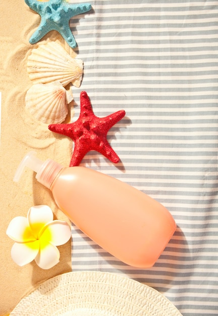 Summer beach, travel, holiday, vacation concept. Tube of sunscreen, starfish, plumeria frangipani and seashells on the sand. Top view. Copy space.