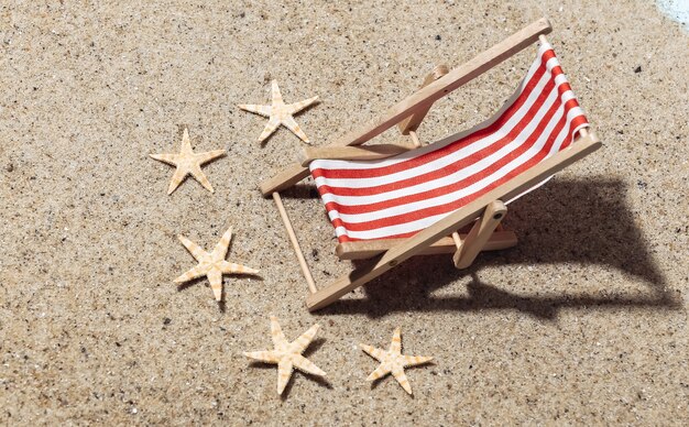 Concetto di vacanza di viaggio di estate spiaggia. mini sedia a sdraio da spiaggia sulla sabbia con stelle marine in una luminosa giornata di sole.