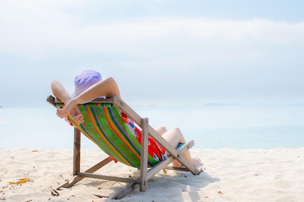 写真 夏のビーチでの休暇のコンセプトタイの椅子のビーチでリラックスして腕を上げて帽子をかぶったアジアの女性