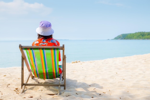 Foto concetto di vacanza estiva in spiaggia donna asiatica con cappello rilassante e braccio su sedia spiaggia in thailandia