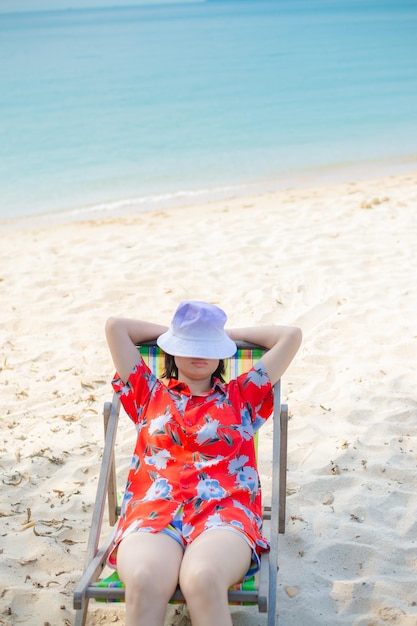 Концепция летнего пляжного отдыха Азиатская женщина в шляпе расслабляется и поднимает руку на стульчике на пляже в Таиланде