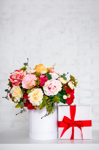 Summer bouquet of beautiful flowers and gift box on the table over white wall background with copy space