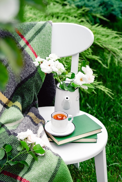 Summer breakfast in garden Cup of tea on books flowers white wild rose in vase teapot warm plaid