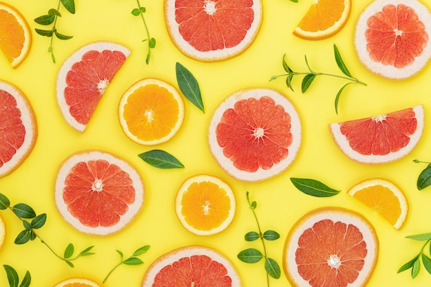 Summer bright background with oranges grapefruits and green leaves on the yellow surface