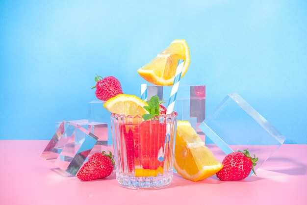 Summer bright lemonade on colorful blue pink background with glass pedestals podiums with fresh fruits, copy space