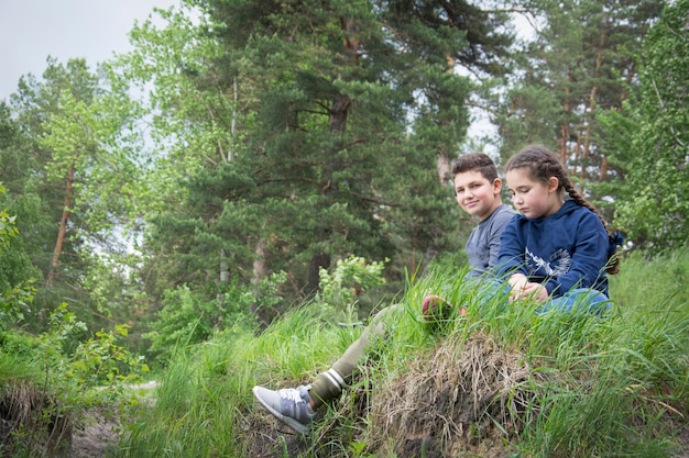 In summer a brother and sister sit on the river bank