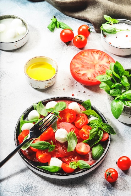 Summer caprese salad with red tomatoes and white mozzarella cheese with fresh green basil leaves Gray table Top view