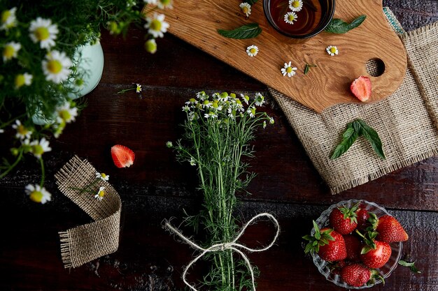 Summer chamomile flowers fresh strawberries herbal tea and mint on sacking on wooden table Aesthetic atmospheric summer lifestyle Beautiful food