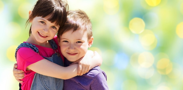 summer, childhood, family, friendship and people concept - two happy kids hugging over green summer lights background