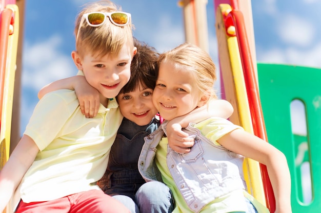 summer, childhood, leisure, friendship and people concept - group of happy kids hugging on children playground