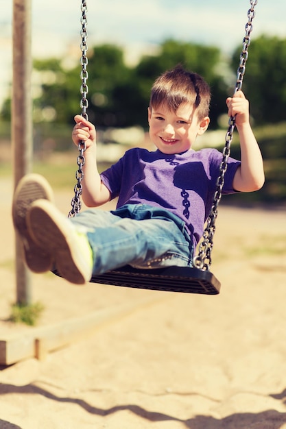 Photo summer, childhood, leisure, friendship and people concept - happy little boy swinging on swing at children playground