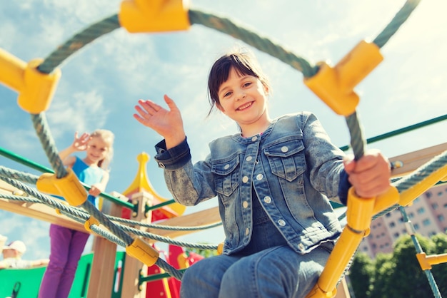 summer, childhood, leisure, gesture and people concept - happy little girl waving hand on children playground climbing frame