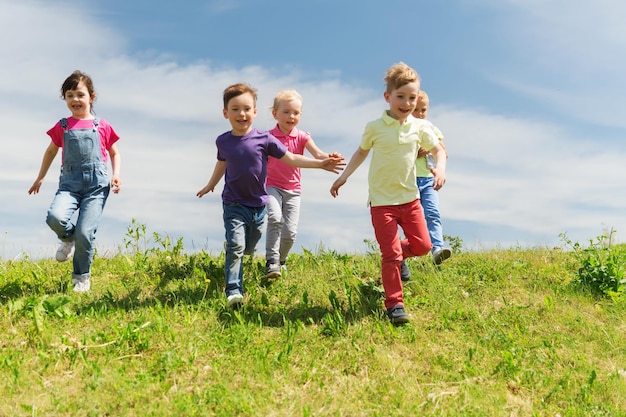 summer, childhood, leisure and people concept - group of happy kids playing tag game and running on green field outdoors