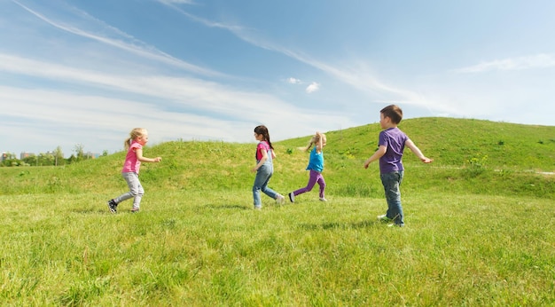 summer, childhood, leisure and people concept - group of happy kids playing tag game and running on green field outdoors