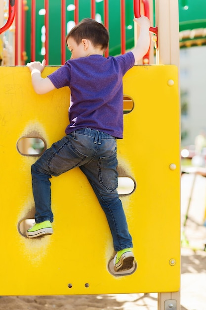 Concetto di estate, infanzia, tempo libero e persone - ragazzino felice sul parco giochi per bambini struttura da arrampicata dal retro