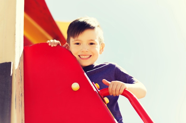 лето, детство, отдых и концепция людей - счастливый маленький мальчик на детской площадке для скалолазания