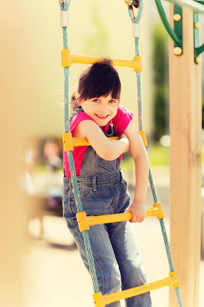 夏、子供時代、レジャー、人々 のコンセプト - ロープはしごで登る子供の遊び場で幸せな少女