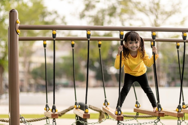 夏の子供の頃のレジャーと人々は子供の遊び場の登山フレームで幸せな少女をコンセプトします