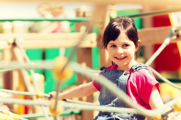 summer, childhood, leisure and people concept - happy little girl on children playground climbing frame