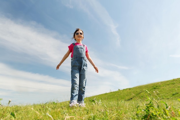 Concetto di estate, infanzia, tempo libero e persone - bambina felice su campo verde e cielo blu all'aperto