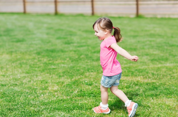 summer, childhood, leisure and people concept - happy little girl running on green summer field