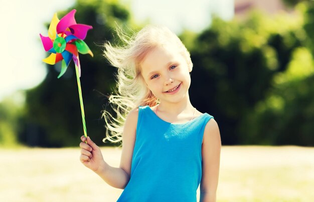 summer, childhood, leisure and people concept - happy little girl with colorful pinwheel toy outdoors