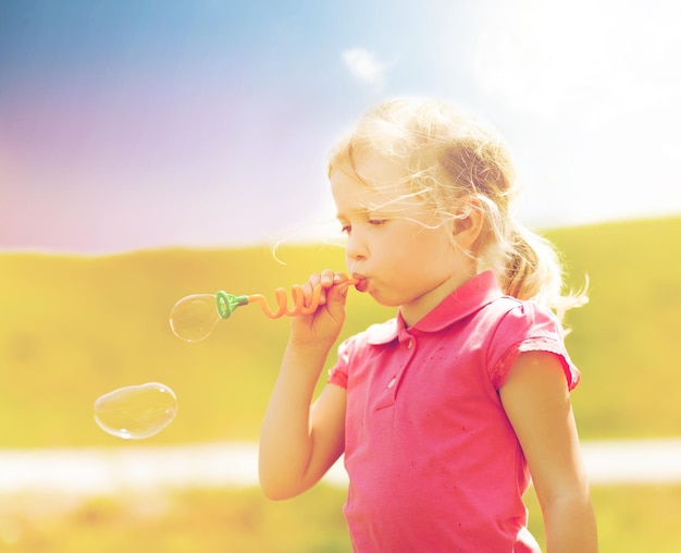 summer, childhood, leisure and people concept - little girl blowing soap bubbles outdoors