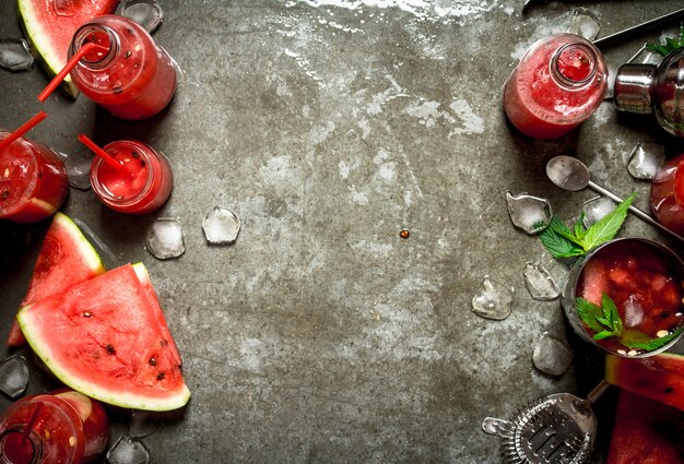Летний коктейль. Ломтики арбуза с мятой и льдом в шейкере на каменном столе.