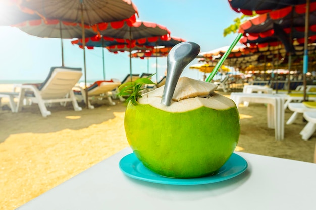 Летний кокосовый коктейль на пляже с пляжными стульями и зонтиками на берегу моря