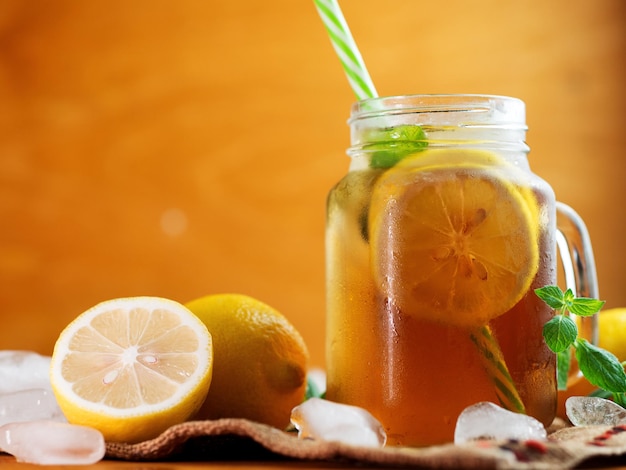 Tè nero freddo estivo con limone e menta in un barattolo su un tavolo di legno