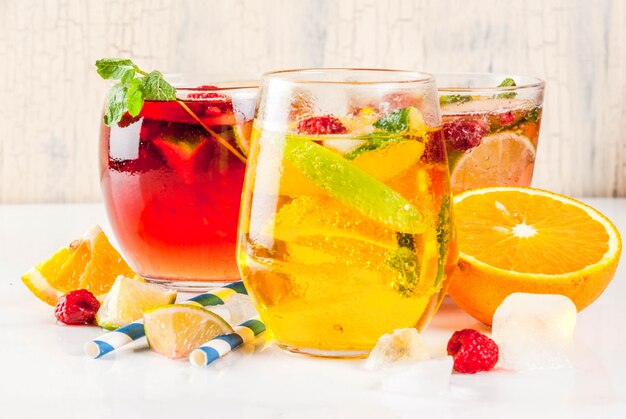 3つのフルーツとベリーのサングリア飲み物の夏の冷たいカクテルセット。アップルレモンオレンジとラズベリーと赤白ピンク。明るい背景