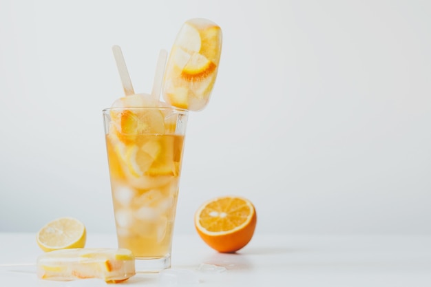 夏の冷たい飲み物柑橘系の果物のカクテルオレンジとレモン、スティックに氷とアイスキャンディー