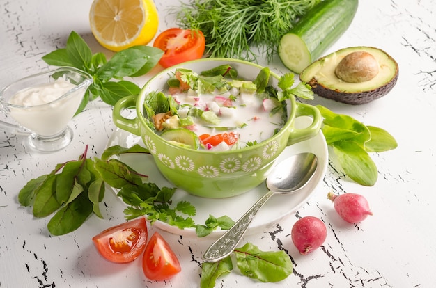 Summer cold raw food soup, okroshka in bowl on white wooden background