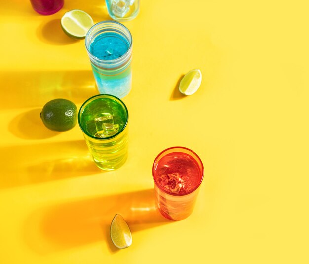 Summer cold refreshing beverage drinks cocktails lemonade in colorful glasses with lime slices on yellow background Top view