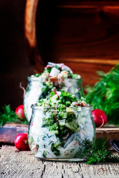 Summer cold soup with vegetables herbs and yogurt in glass jars rustic style vintage wooden background