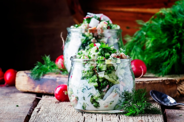 Summer cold soup with vegetables herbs and yogurt in glass jars rustic style vintage wooden background