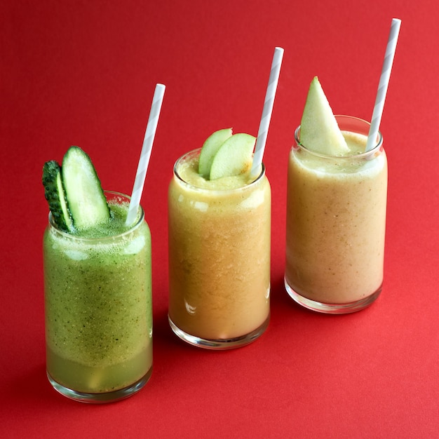 Summer colorful fruit cocktails smoothies on a red surface.