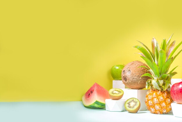 Summer composition, Various tropical fruits, on modern bright yellow background with podiums, copy space. Holiday and vacation, healthy food concept copy space