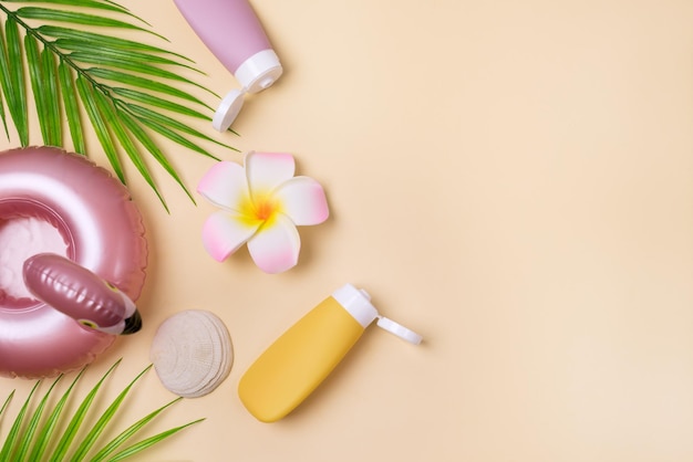 Summer composition with sunblock lotion bottles palm leaf sea shells and plumeria on pink background