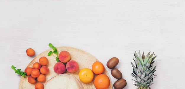 Summer concept banner female hat with fruit on wooden table top view